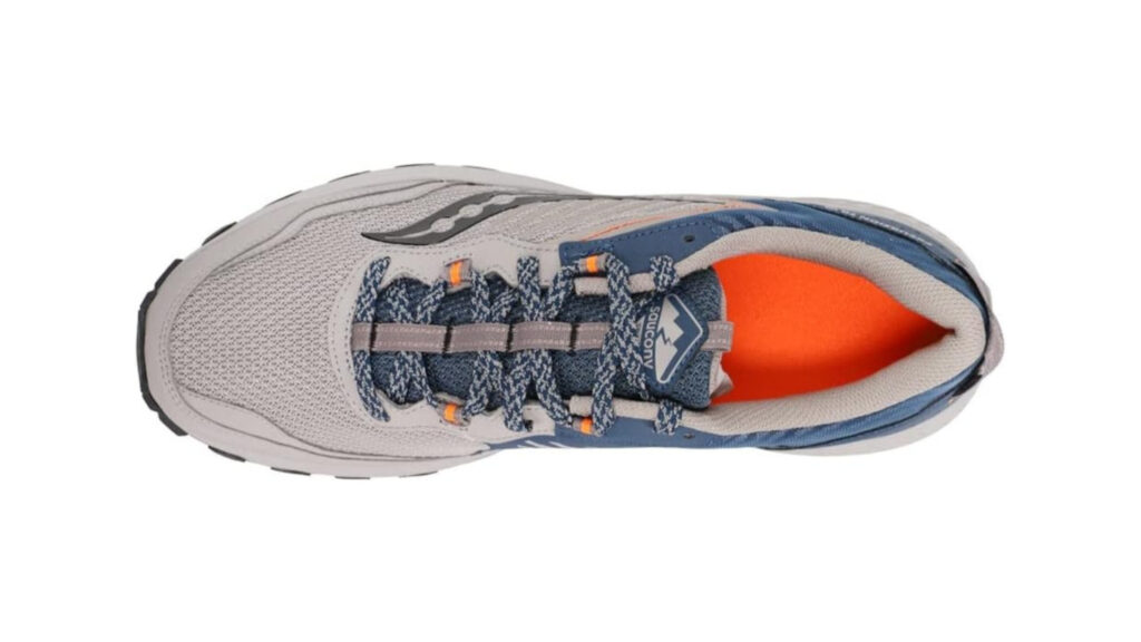 A rugged Saucony TR15 trail running shoe standing on a rocky, uneven trail. The shoe is illuminated by warm, directional lighting, casting dramatic shadows that emphasize its technical features and durable construction. The foreground is in sharp focus, while the middle ground shows a winding path disappearing into a lush, verdant forest in the distance. The atmosphere conveys a sense of adventure and the shoe's ability to provide reliable performance on challenging terrain.